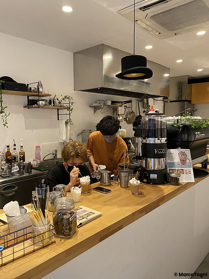 Due persone lavorano dietro il bancone in legno di Hatcoffee ad Asakusa, preparando bevande con latte art.