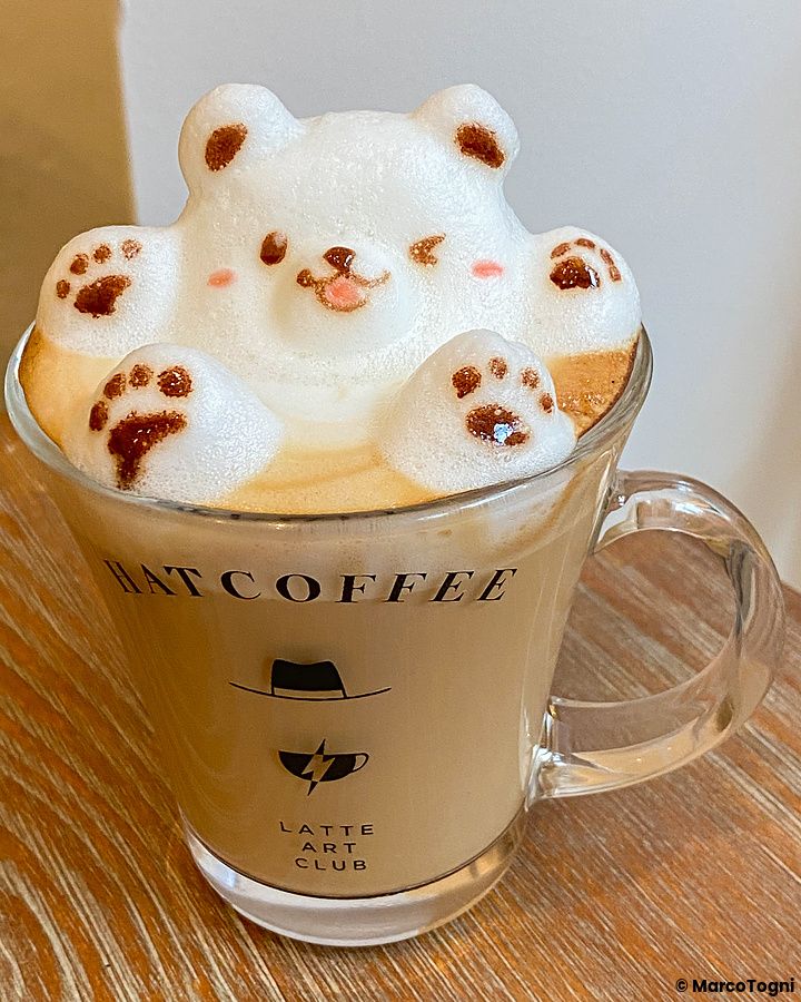 Un cappuccino in una tazza con il logo Hatcoffee presenta una decorazione in schiuma di latte a forma di orsetto.