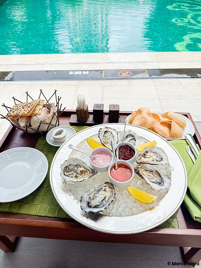 Piatto di ostriche crude con salse e limone vicino alla piscina.