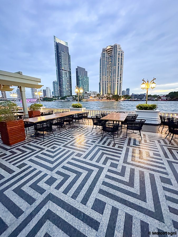 Tavoli e sedie nella zona piscina al Mandarin Oriental Bangkok con skyline sullo sfondo.