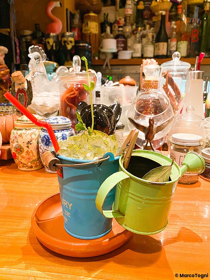 Un cocktail servito in un secchiello blu con un annaffiatoio verde decorativo sopra il bancone del Orchard Bar a Ginza.