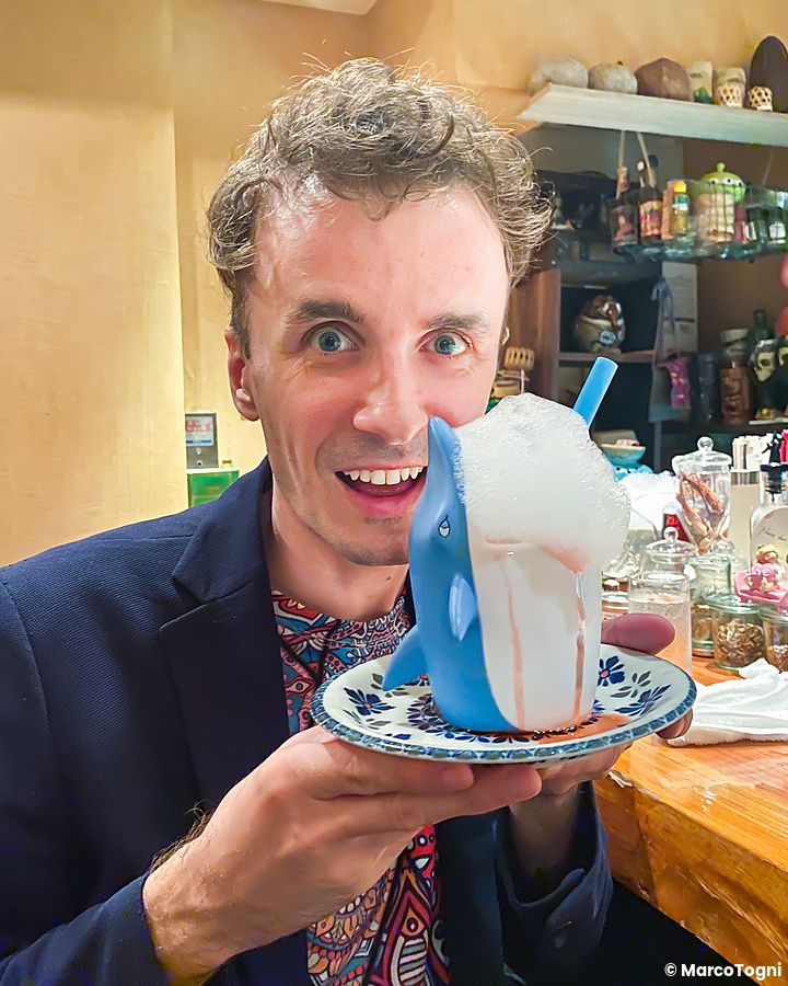 Marco Togni mostra un cocktail in bicchiere a forma di squalo a Orchard Bar, servito su un piattino decorato.