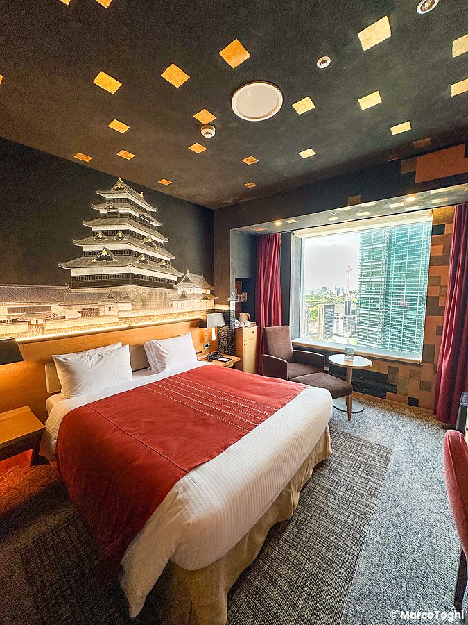 Una stanza artistica a Park Hotel Tokyo con murale di un castello giapponese e vista su grattacieli.