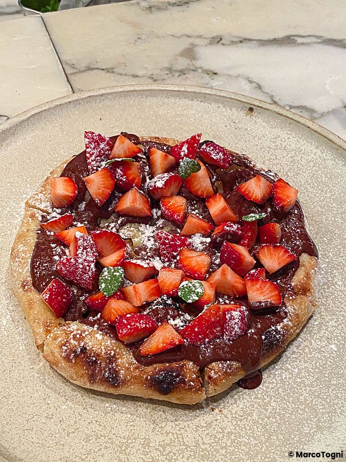 Una pizza dolce con fragole e cioccolato spolverata di zucchero a velo su un piatto chiaro, servita a Tokyo.