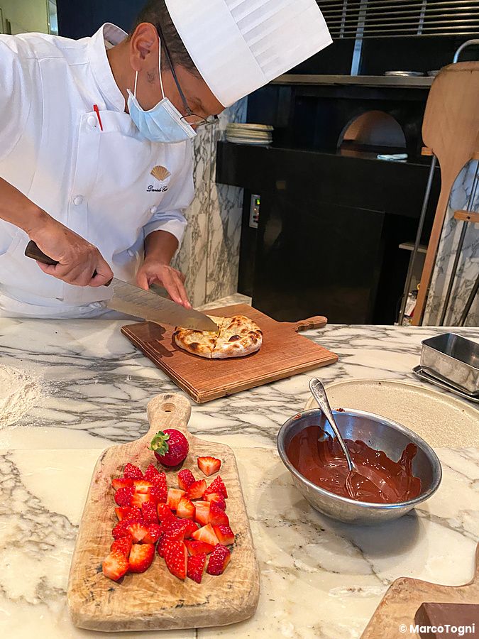 Un pizzaiolo taglia una base di pizza su un tagliere in una cucina professionale a The Pizza Bar On 38th a Tokyo.