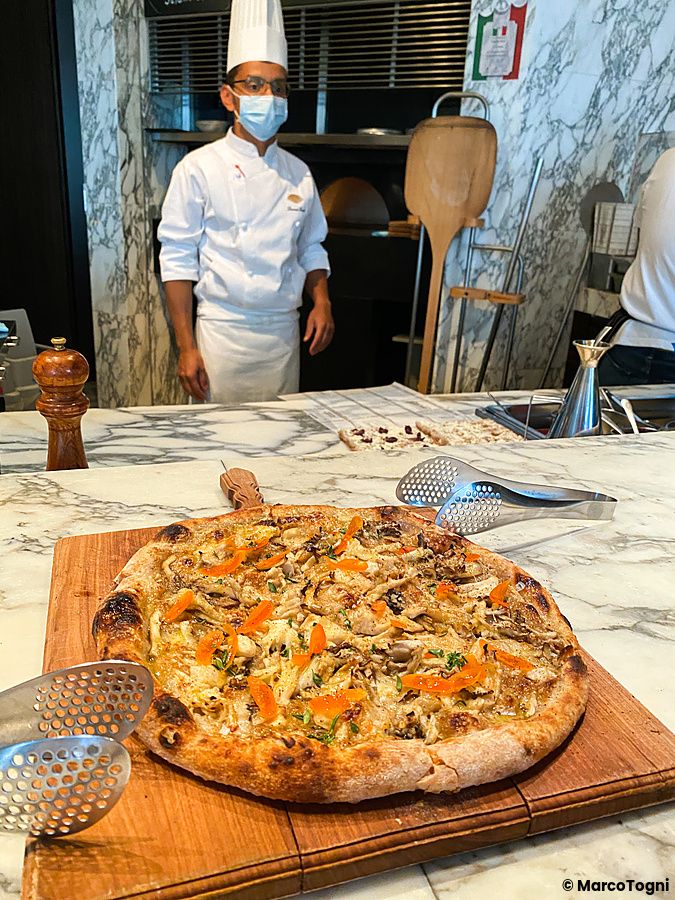 Pizza ai funghi su tagliere di legno presso The Pizza Bar On 38th, con uno chef sullo sfondo.