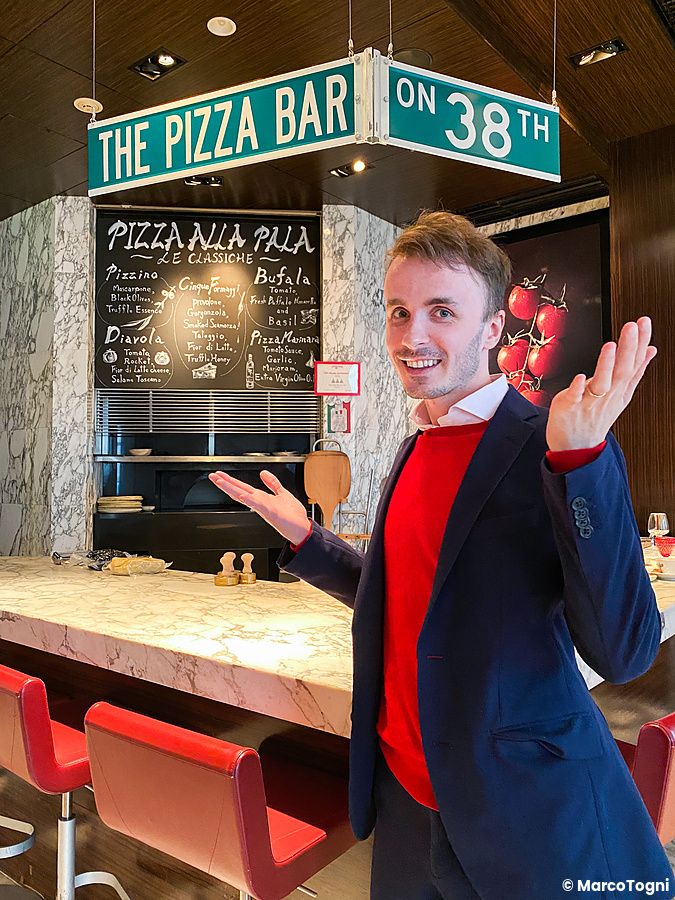 Marco Togni sorridente posa nel ristorante a The Pizza Bar On 38th davanti al bancone in marmo.