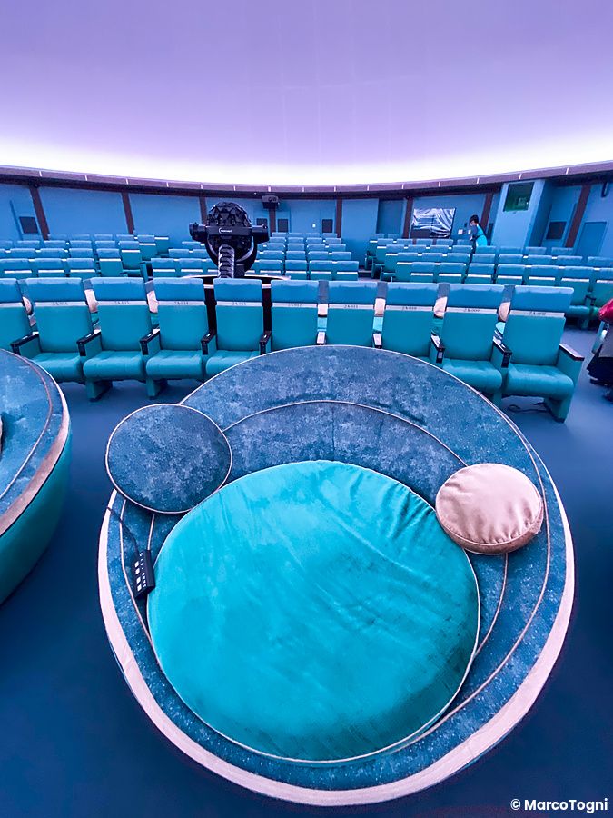 Interno della sala di proiezione del Konica Minolta Planetaria Tokyo con file di sedute azzurre e una poltrona circolare.