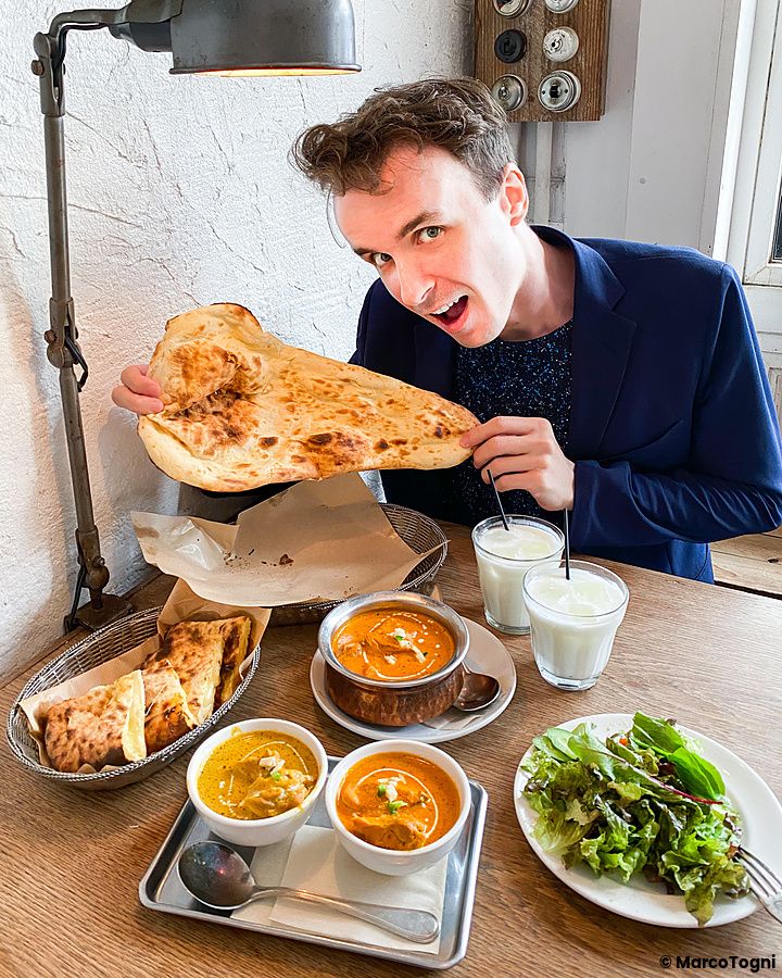 Marco Togni sorridente tiene in mano un pezzo di pane naan in un tavolo imbandito presso il ristorante Sajilo Clove.