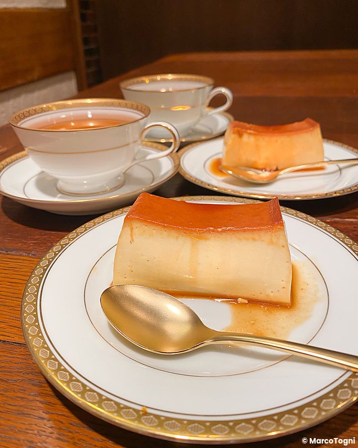 Due porzioni di budino caramellato con cucchiaini dorati su piattini in porcellana presso la caffetteria Satella a Shibuya.