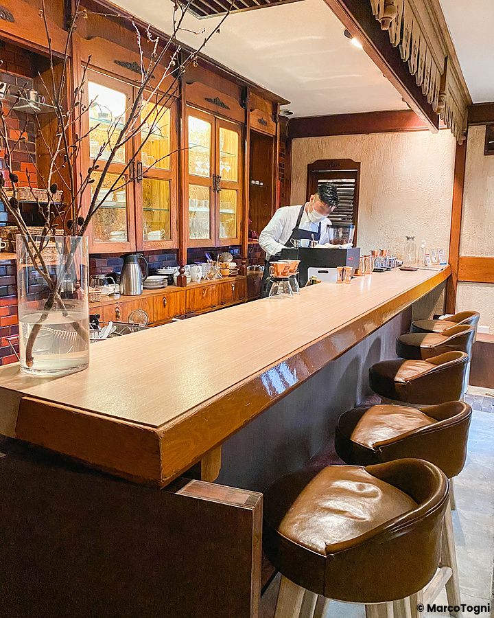L'interno della caffetteria Satella a Shibuya con un bancone in legno, sgabelli in pelle e un uomo al lavoro.