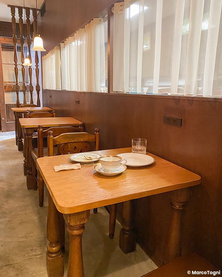 Interno della caffetteria Satella a Shibuya con tavoli in legno, tende bianche e stoviglie usate sopra un tavolino.