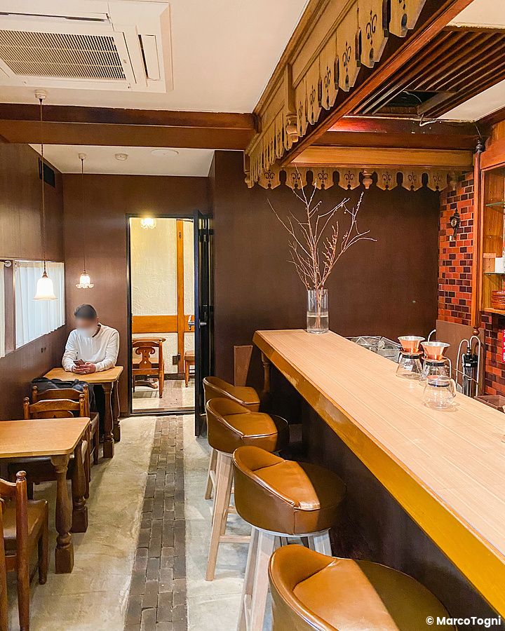 L'interno della caffetteria Satella a Shibuya con un bancone in legno, sgabelli e un cliente seduto ai tavoli.