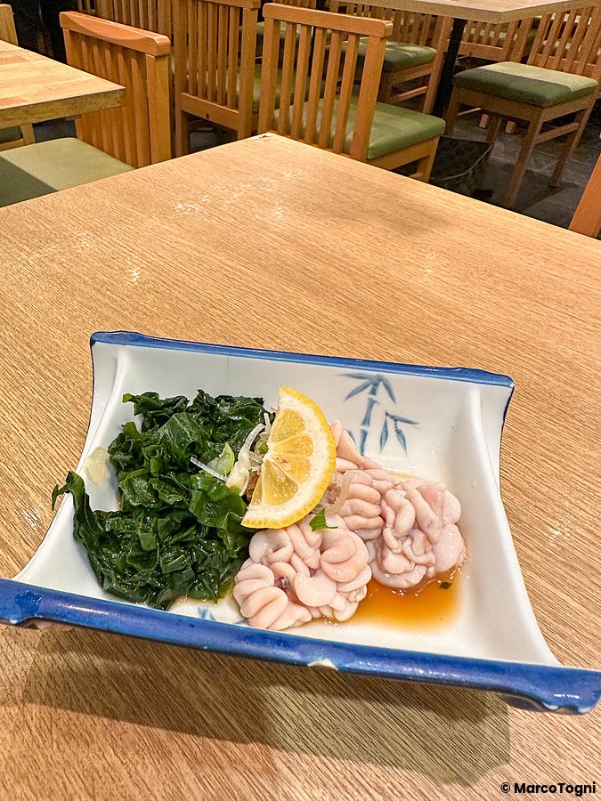 Un piatto con shirako e alghe wakame servito su una tavola di legno presso il ristorante Sushi no Darihan a Shinjuku.