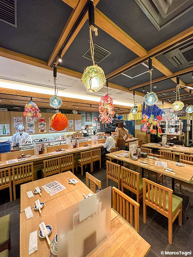 Interno del ristorante Sushi no Darihan a Shinjuku con tavoli in legno, bancone e decorazioni a sospensione colorate.