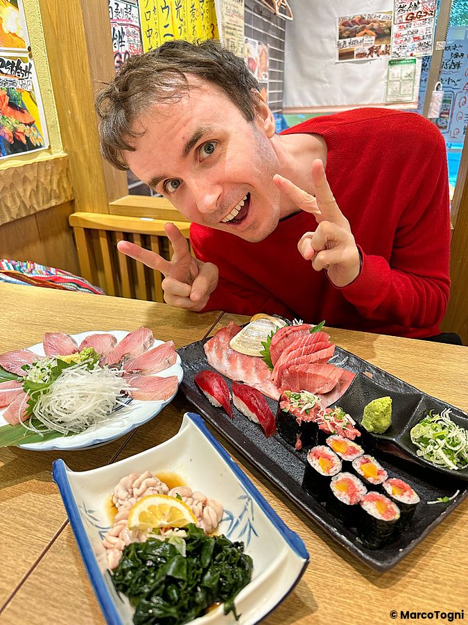 Marco Togni sorridente con sushi e sashimi su un tavolo al Sushi no Darihan.