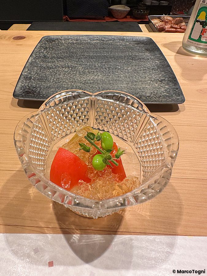 Un antipasto a Sushi Punch servito in una coppetta di vetro con pomodori, edamame e gelatina su un tavolo in legno.