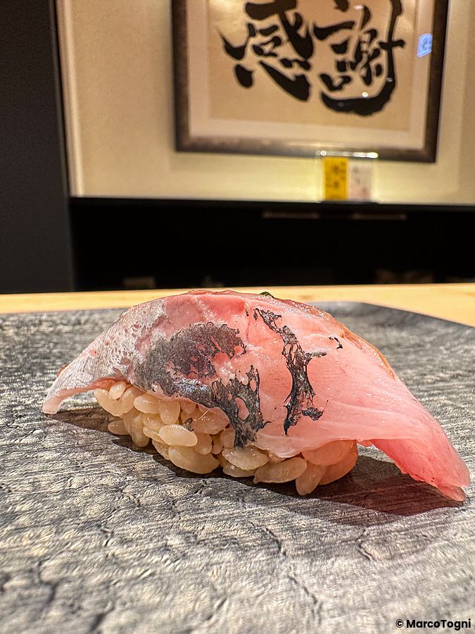 Un nigiri di aji servito su un piatto in pietra grigia da Sushi Punch a Tokyo.