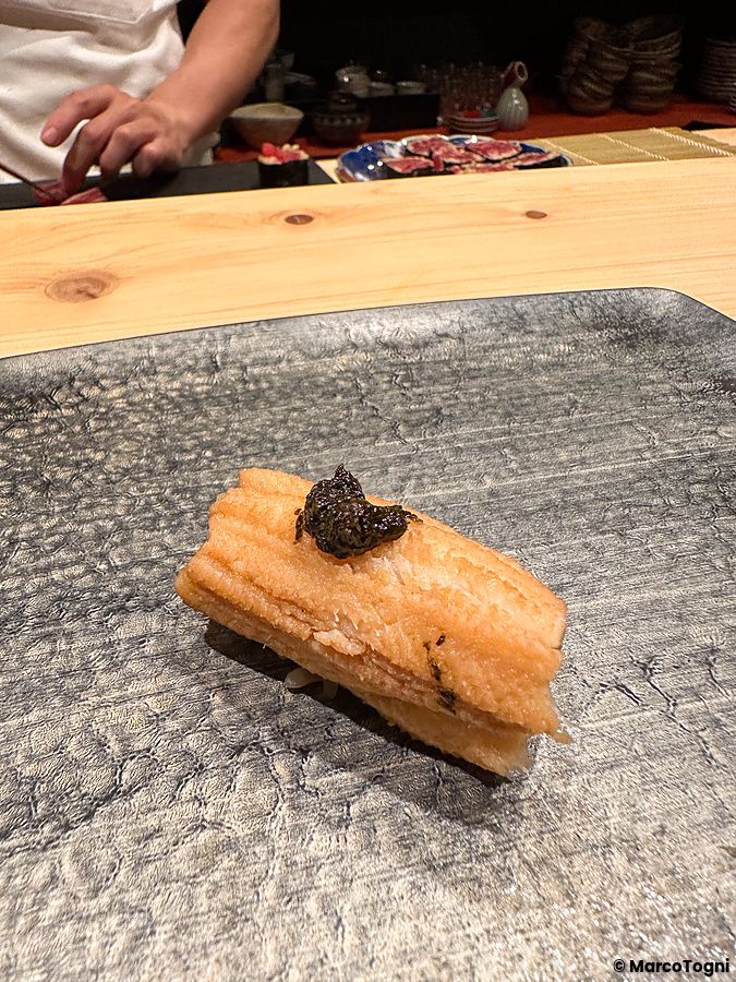 Un nigiri di anago con guarnizione posato su un piatto di ceramica scura presso il ristorante Sushi Punch a Tokyo.