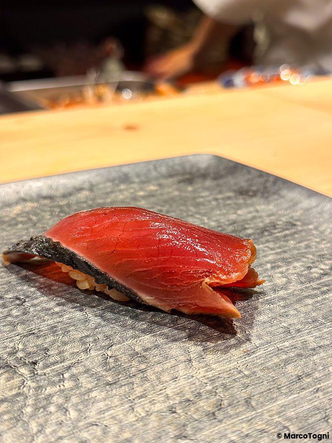 Un nigiri di katsuo servito su un piatto di pietra scura da Sushi Punch a Tokyo.