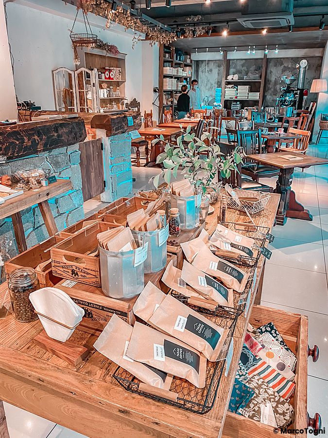 Esposizione di caffè in grani e prodotti del Takao Coffee su un banco in legno all'interno della torrefazione a Hachioji.