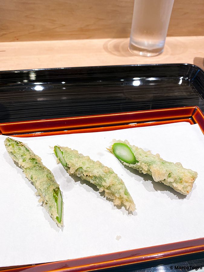 Tre pezzi di asparagi a Tempura Kondo, serviti su carta bianca all'interno di un vassoio laccato nero a Ginza.