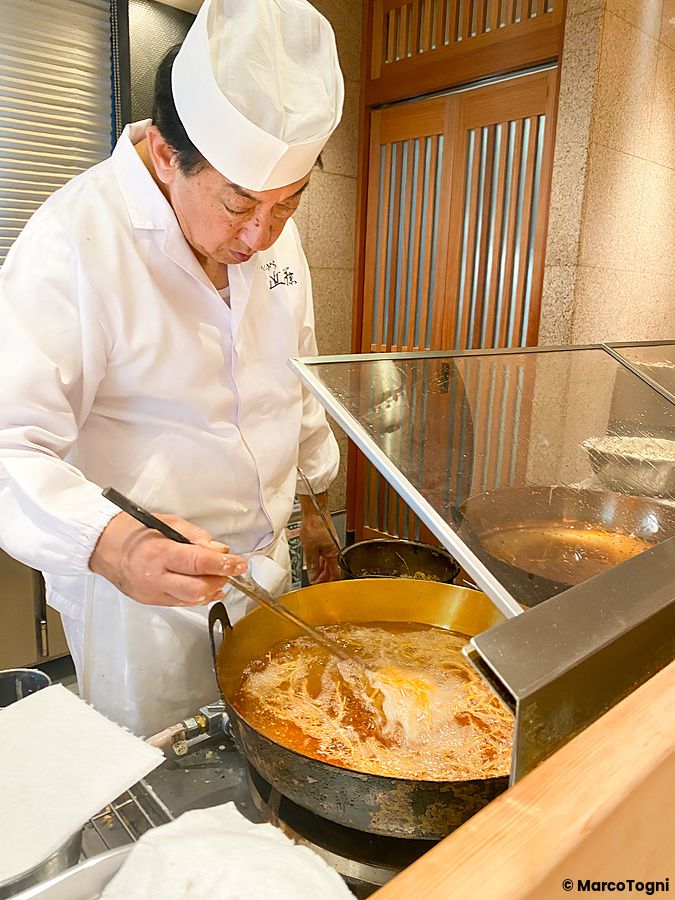 Uno chef all'opera a Tempura Kondo mentre frigge la tempura in una pentola posizionata sul bancone del ristorante.