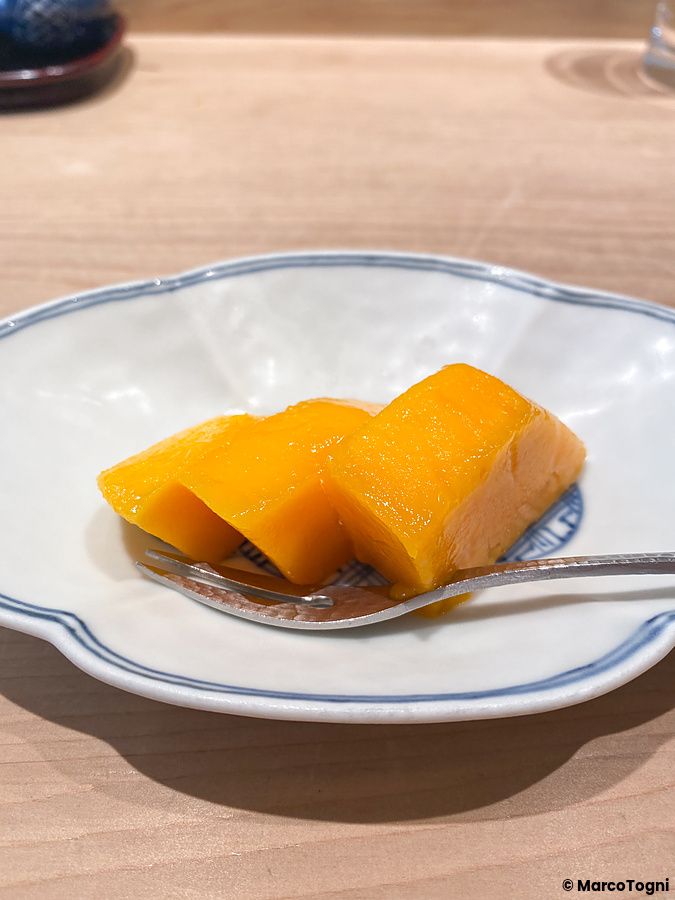 Tre fette di mango servite su un piatto di ceramica bianca con bordo blu presso il ristorante Tempura Kondo a Ginza.
