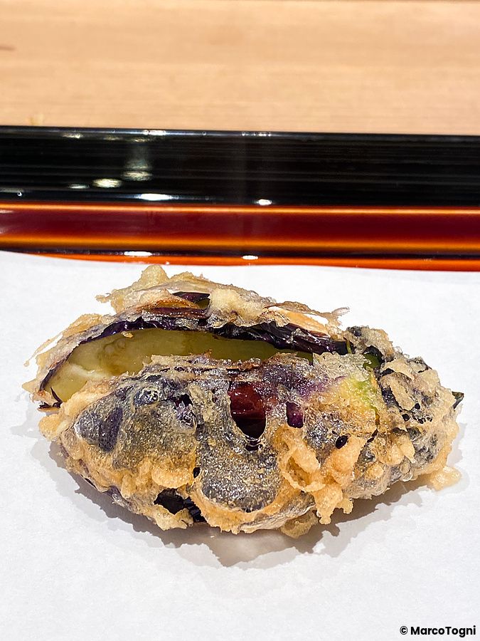 Una melanzana a Tempura Kondo fritta in pastella dorata, servita su carta bianca in un ristorante di Ginza a Tokyo.