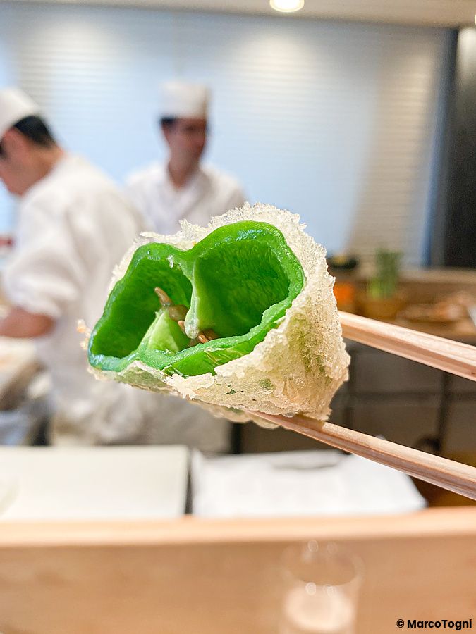 Un peperone dolce a Tempura Kondo fritto in pastella croccante, tenuto con le bacchette all'interno del ristorante.
