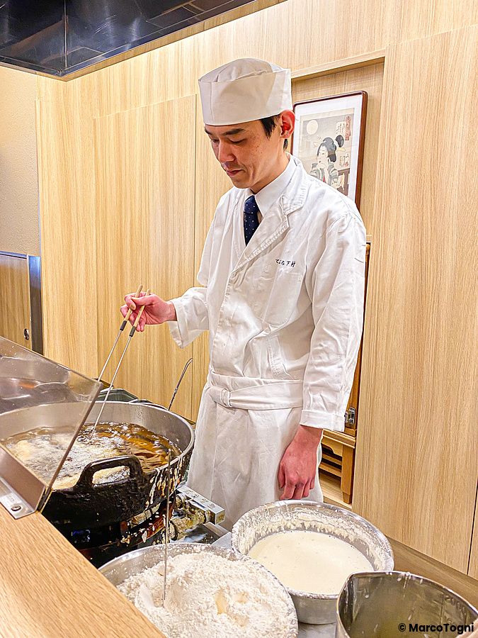 Uno chef a Tempura Shimomura, un uomo in divisa bianca, frigge in olio bollente in un ristorante di Tokyo.