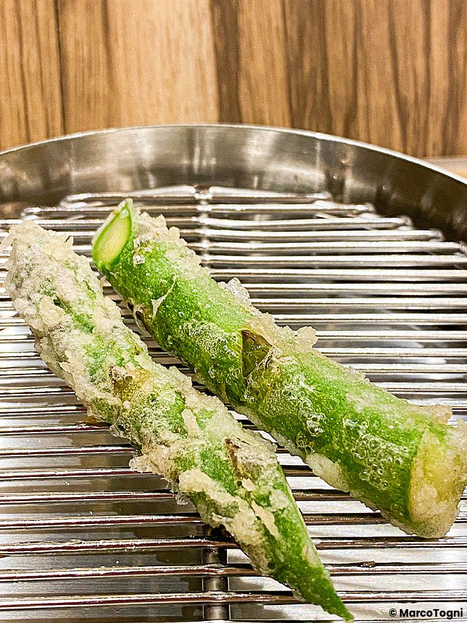 Due asparagi fritti in tempura posati su una griglia metallica al ristorante Tempura Shimomura di Tokyo.