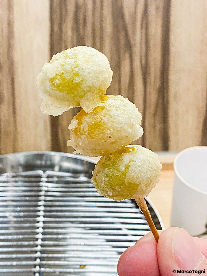 Uno spiedino con tre frutti di ginkgo in tempura tenuto da una persona presso il ristorante Tempura Shimomura a Tokyo.