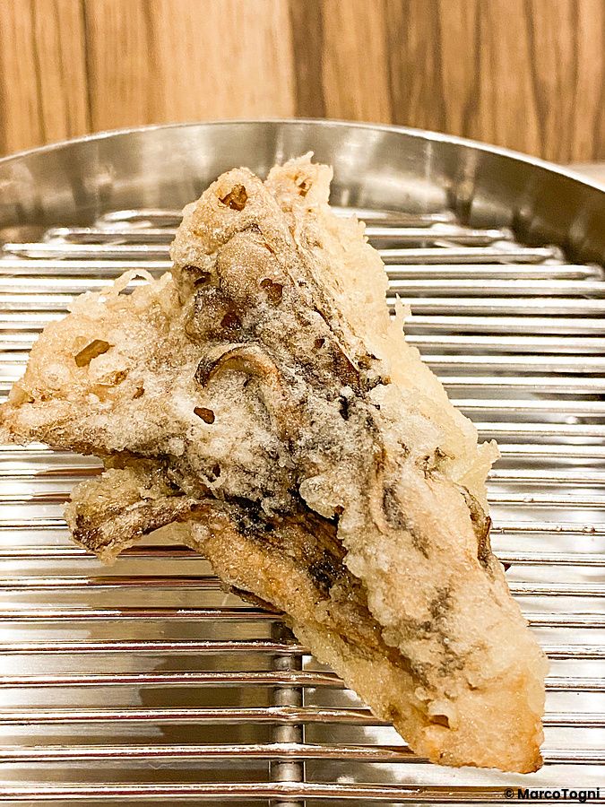 Tempura di fungo maitake fritta e dorata adagiata su una griglia metallica presso il ristorante Tempura Shimomura.