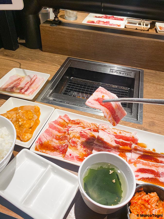 Una fetta di carne cruda sollevata con le bacchette sopra una griglia presso il ristorante Yakiniku Like.