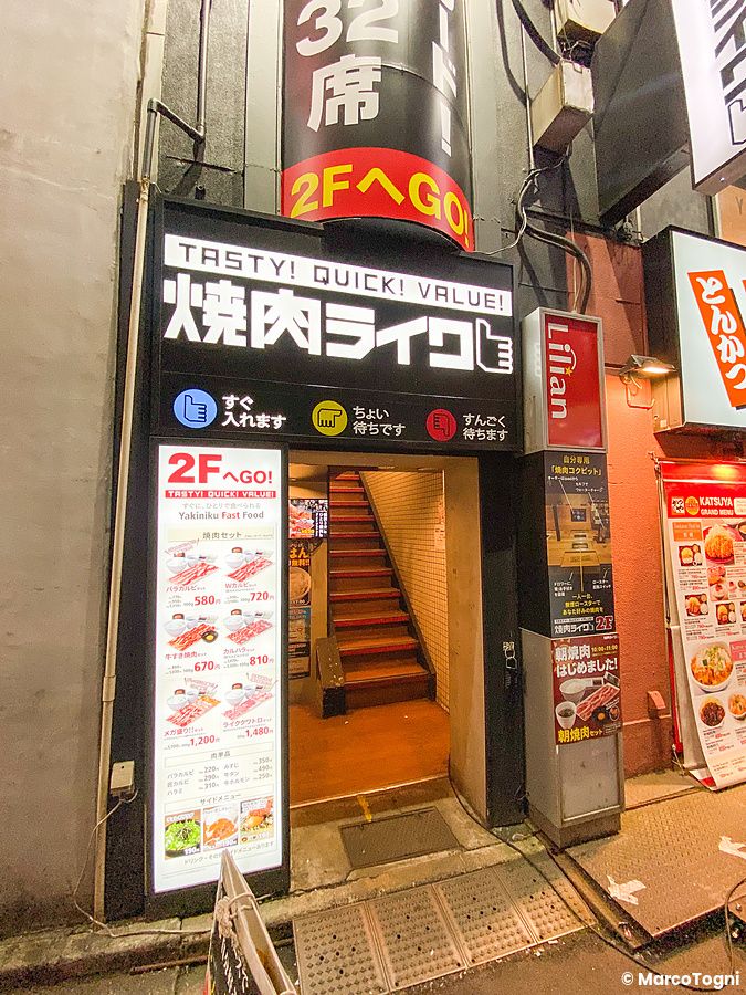 L'ingresso, sede di Akihabara a Yakiniku Like, con una scala interna e insegne del menu su sfondo scuro.