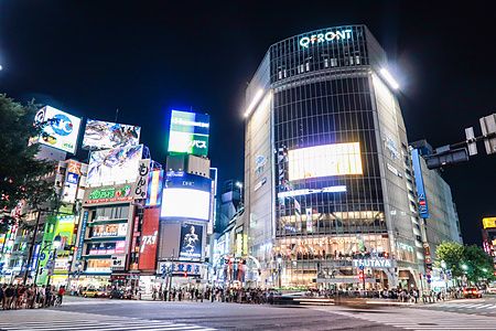 Incrocio di Shibuya di notte con luci al neon e cartelloni pubblicitari.