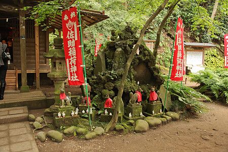 Statue decorate con tessuti rossi al Sasuke Inari a Kamakura, circondate da vegetazione.