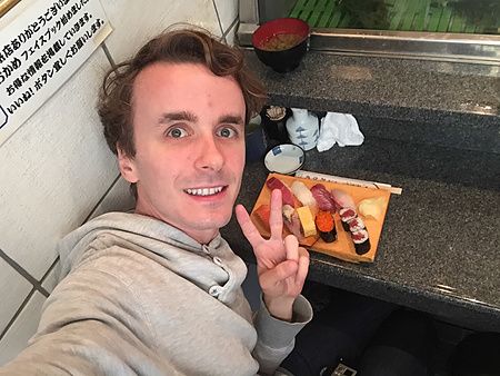 Marco Togni sorridente scatta un selfie al bancone di Sushidokoro Okame a Tokyo, con un vassoio di sushi davanti a sé.