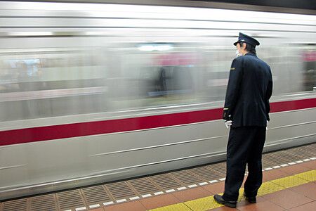 Addetto alla sicurezza osserva un treno in movimento in una stazione in Giappone.