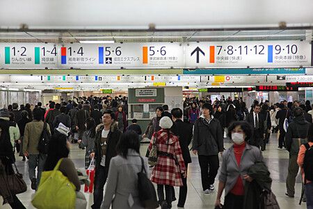 Una folla di persone cammina in un corridoio della stazione Shinjuku a in Giappone sotto la segnaletica dei binari.