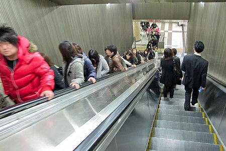 Diverse persone in abbigliamento invernale utilizzano una scala mobile giappone all'interno di una stazione in Giappone.