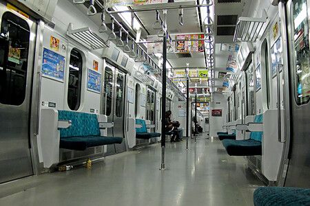 Interno di un vagone deserto della linea Yamanote in Giappone con sedili blu e una persona seduta in fondo.