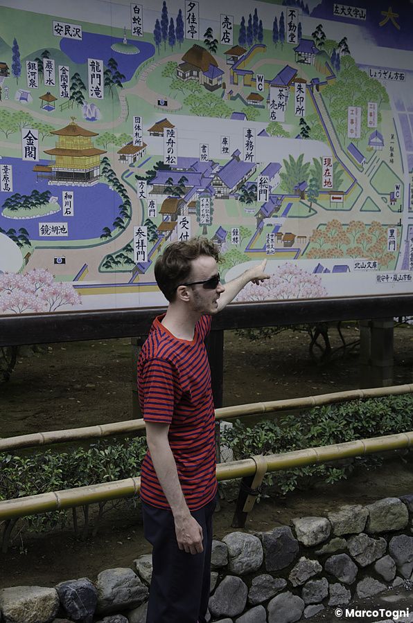 Un turista uomo indica una mappa turistica all'interno del complesso del Kinkaku-ji a Tokyo.