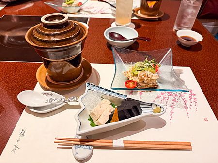 Antipasti a Ume no Hana a Ginza serviti in raffinati piatti di ceramica e vetro su una tovaglietta illustrata.