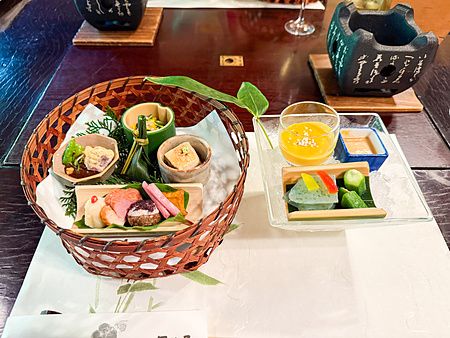 Un cestino con antipasti a Kurochaya, con piccole porzioni disposte in recipienti di bambù e ceramica su un tavolo.