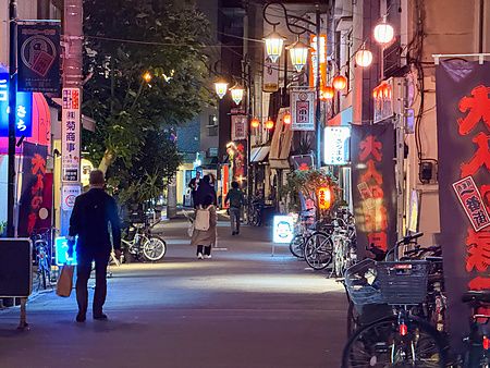 Veduta notturna di una strada nel quartiere di Asagaya a Tokyo con lanterne e persone che camminano tra le biciclette.