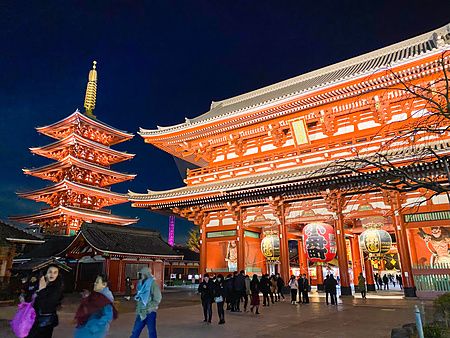 Vista notturna del tempio Senso-ji ad Askausa con la porta Hozomon e la pagoda illuminate e persone nel piazzale.