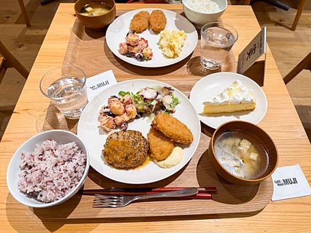 Un set completo a Cafe＆Meal Muji con piatti assortiti, riso, zuppa di miso e un dolce su un tavolo in legno.