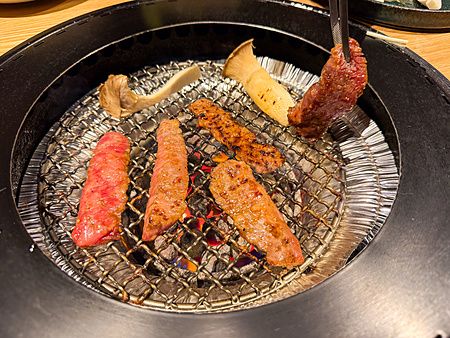 Tagli di carne e funghi che cuociono su una griglia circolare all'interno del Ristorante Toraji.